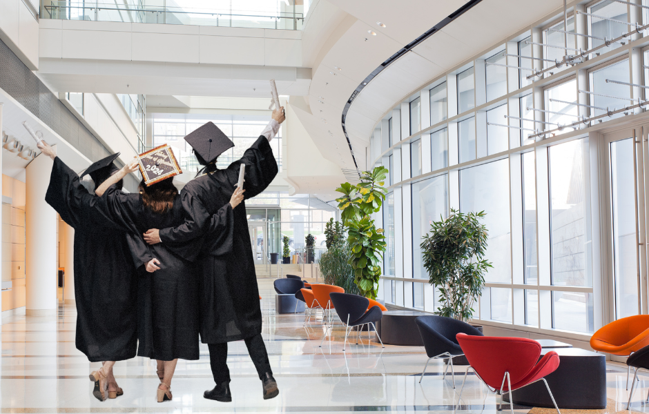 Three recent graduates in caps and gowns celebrating in an office building